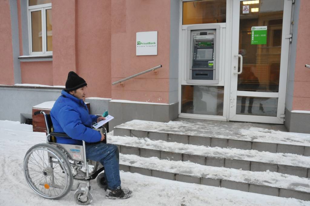 Vladimirs Ivanovs pie “Privatbank” Liepājas filiāles Graudu ielā vispirms sagaida, kad kāds pasauks bankas darbinieku, tad iedod norēķinu karti naudas izņemšanai, rēķinu apmaksai un gaida, kad viss tiks izdarīts. “Te līdz bankai var ērti nokļūt. Var arī veikalos iebraukt, iepērkos, uzpīpēju, kamēr gaidu. Šodien jau ir silts! Kur netieku, tur cilvēki palīdz,” spriež V. Ivanovs.
Autors: Dainis Ģelzis